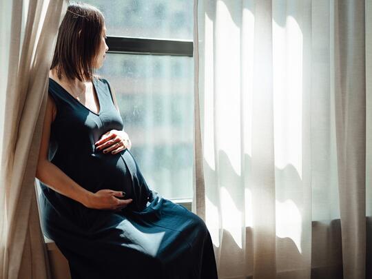 Gravid kvinne sitter i vinduskarm og ser ut